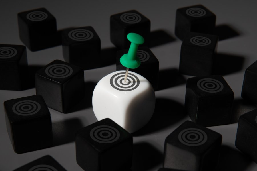 A white cube with a target and a green pushpin stands out among a black cubes. Goal setting, target setting, focus concept.