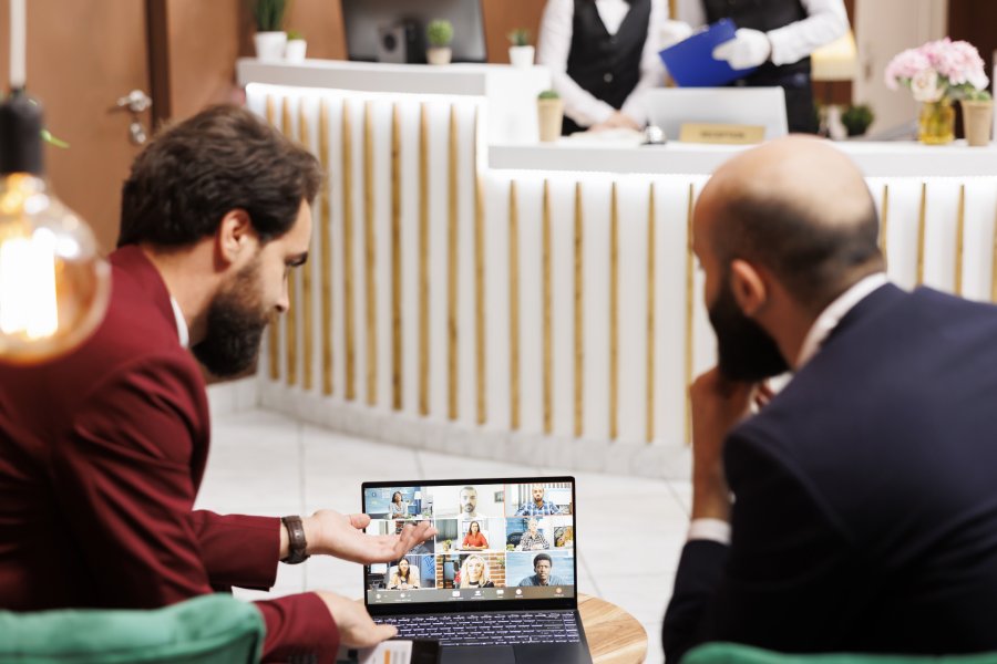 Business partners meet with people on videocall in hotel lobby, attending online teleconference chat to share project ideas, travelling for work. Entrepreneurs working with videoconference.